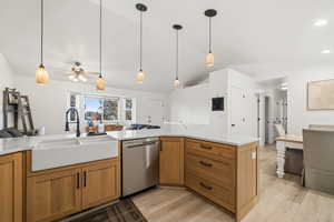 Kitchen with open floor plan, vaulted ceiling, stainless steel dishwasher, light wood finished floors, and decorative light fixtures