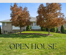 View of property hidden behind natural elements with brick siding, a front yard, and a shingled roof