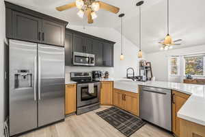 Kitchen featuring a ceiling fan, appliances with stainless steel finishes, decorative light fixtures, vaulted ceiling, and light wood-style floors