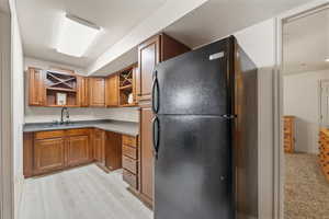 Kitchen with freestanding refrigerator, brown cabinetry, open shelves, light wood-style floors, and dark stone countertops