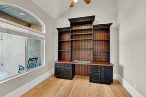 Unfurnished office with built in desk, vaulted ceiling, light wood-style floors, and a ceiling fan