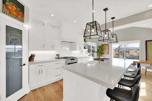 Kitchen featuring white cabinetry, a kitchen island with sink, pendant lighting, a breakfast bar area, and light stone countertops