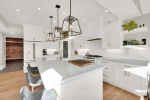 Kitchen featuring open shelves, high end appliances, a kitchen breakfast bar, hanging light fixtures, and white cabinets