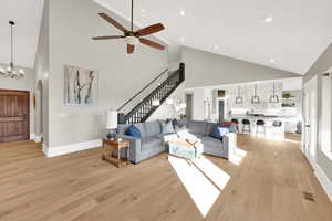 Living area with high vaulted ceiling, light wood finished floors, ceiling fan, stairway, and arched walkways