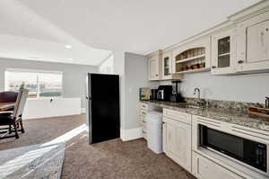 Kitchen featuring dark stone counters, stainless steel appliances, dark colored carpet, glass insert cabinets, and cream cabinets