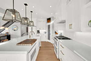 Kitchen featuring white appliances, white cabinets, light stone countertops, a large island with sink, and pendant lighting