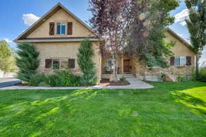 Back of house with stone siding, stucco siding, and a yard