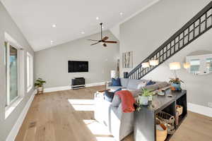 Living area with high vaulted ceiling, light wood finished floors, ceiling fan, recessed lighting, and stairs