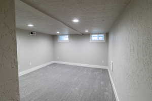 Below grade area featuring light carpet, recessed lighting, a textured wall, and a textured ceiling