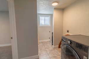 Laundry area featuring a textured wall, washer / dryer, a textured ceiling, and light tile patterned flooring