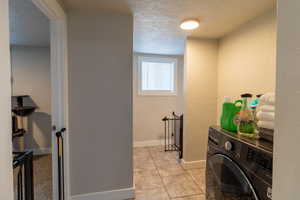 Laundry room with a textured ceiling, washer / dryer, a textured wall, and light tile patterned floors