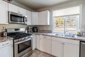 Kitchen featuring appliances with stainless steel finishes, white cabinets, and light tile patterned flooring