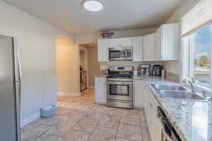 Kitchen featuring appliances with stainless steel finishes, arched walkways, white cabinets, light stone counters, and light tile patterned floors