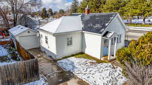 View of snowy exterior with a chimney and a shingled roof