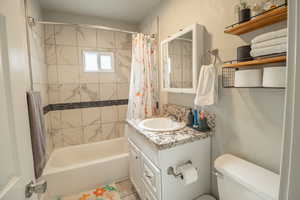 Full bath with a textured wall, shower / bath combo with shower curtain, and vanity