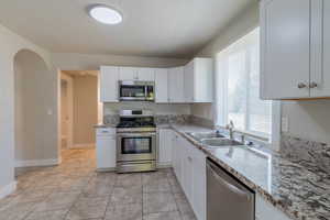 Kitchen with stainless steel appliances, white cabinets, arched walkways, light stone counters, and light tile patterned floors