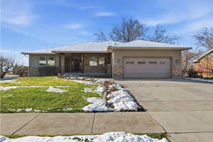 View of front of house featuring concrete driveway, an attached garage, a lawn, stone siding, and stucco siding