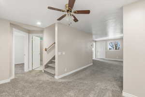 Empty room featuring light carpet, stairway, and ceiling fan