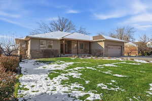 Single story home with stone siding, an attached garage, stucco siding, a lawn, and driveway