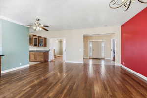 Unfurnished living room featuring dark wood-style floors, ceiling fan, and a chandelier