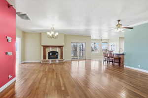 Living room featuring a fireplace, light wood finished floors, a chandelier, and a ceiling fan