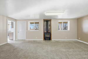 Unfurnished living room featuring a wood stove, healthy amount of natural light, carpet floors, and a textured ceiling