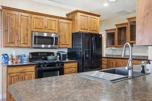 Kitchen with dark countertops, black appliances, brown cabinets, glass insert cabinets, and recessed lighting