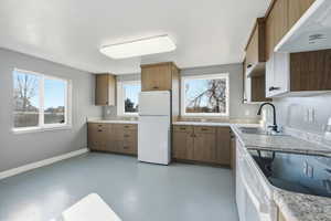 Kitchen featuring white appliances, under cabinet range hood, concrete flooring, light countertops, and brown cabinetry