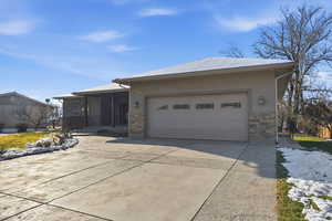 View of front of property featuring stone siding, driveway, a sunroom, an attached garage, and stucco siding