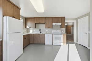 Kitchen with finished concrete flooring, white appliances, under cabinet range hood, and brown cabinets