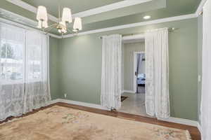 Spare room with wood finished floors, crown molding, and a chandelier