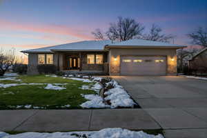 View of front facade featuring covered porch, concrete driveway, a lawn, an attached garage, and stone siding