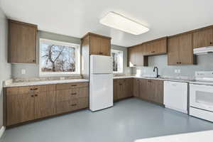 Kitchen featuring concrete floors, white appliances, under cabinet range hood, light stone countertops, and brown cabinets