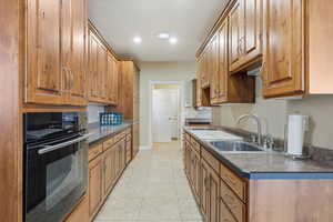 Kitchen with black oven, dark countertops, brown cabinets, light tile patterned floors, and recessed lighting