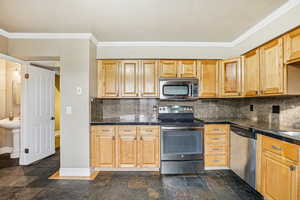 Kitchen featuring tile countertops, stainless steel appliances, stone tile flooring, ornamental molding, and backsplash