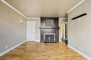 Unfurnished living room with light wood-style floors, a textured ceiling, a fireplace, and crown molding
