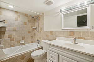 Full bath featuring tiled shower / bath combo, vanity, and tile walls