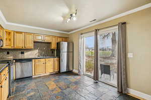 Kitchen with appliances with stainless steel finishes, backsplash, ornamental molding, and stone tile flooring