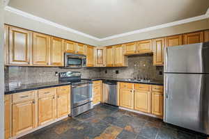 Kitchen featuring stainless steel appliances, crown molding, tile countertops, backsplash, and stone tile flooring