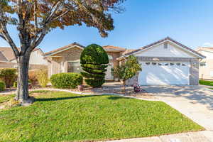 View of front of house featuring concrete driveway, a front yard, brick siding, a garage, and a tiled roof