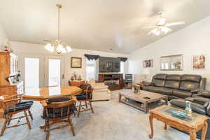 Living room featuring vaulted ceiling, carpet floors, a fireplace, a chandelier, and ceiling fan