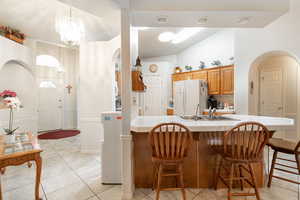 Kitchen featuring arched walkways, tile countertops, freestanding refrigerator, vaulted ceiling, and a breakfast bar