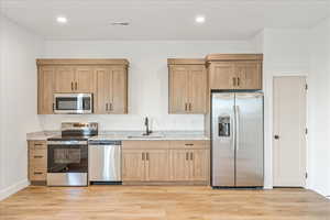 Kitchen featuring stainless steel appliances, light stone countertops, light brown cabinets, light wood-style floors, and recessed lighting