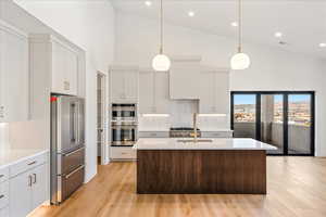 Kitchen featuring high vaulted ceiling, appliances with stainless steel finishes, an island with sink, white cabinets, and pendant lighting