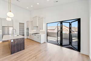 Kitchen featuring a high ceiling, hanging light fixtures, white cabinetry, an island with sink, and stainless steel appliances