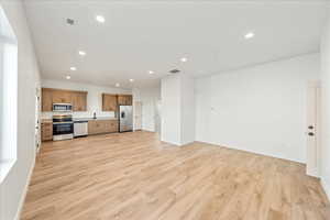 Kitchen with recessed lighting, appliances with stainless steel finishes, brown cabinets, open floor plan, and light wood-style flooring
