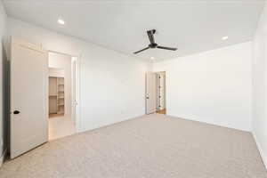 Unfurnished bedroom with light carpet, a spacious closet, recessed lighting, and ceiling fan