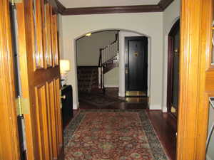 Corridor featuring stairway, crown molding, wood finished floors, and arched walkways