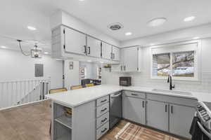 Kitchen with gray cabinetry, backsplash, a peninsula, light stone countertops, and light wood-style floors