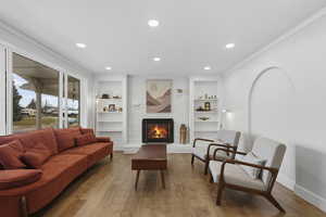 Living area featuring built in shelves, a brick fireplace, wood finished floors, recessed lighting, and crown molding